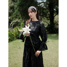 Woman in a black floral blouse by Renaette holding a white flower in a garden setting