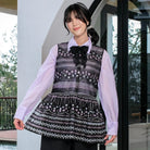Woman wearing a black patterned outer by Holy Peony over a light purple shirt outdoors.