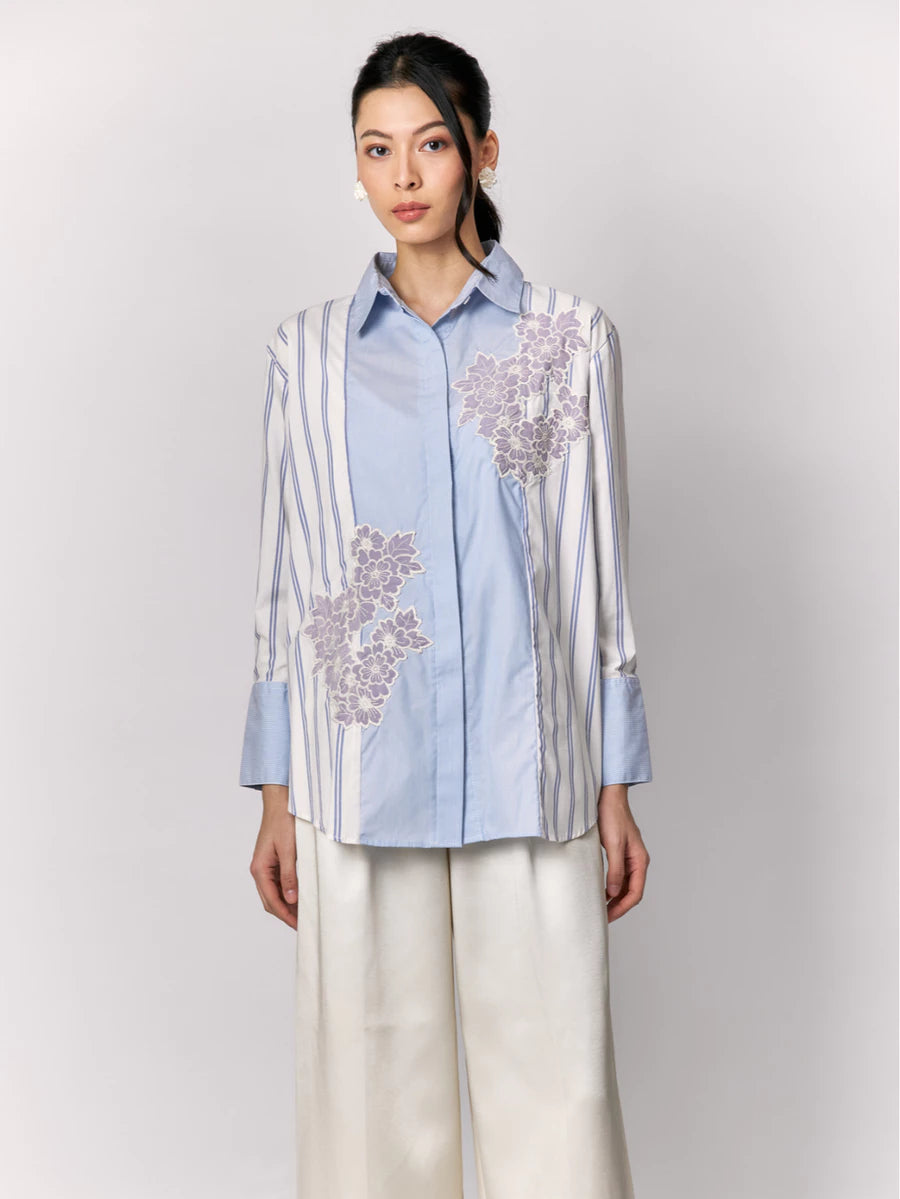 Woman wearing a light blue shirt by Studio Tui with floral embroidery on a plain background