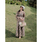 Woman in a ash brown floral outfit with floral embroidery by Renaette holding a basket in a grassy field