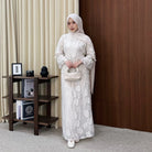 Woman in a white floral outfit by Renaette standing in a room with a wooden side table and books.