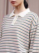 A close-up of a model wearing a long-sleeve polo shirt by Hijabchic with horizontal stripes in green, orange, and black on an off-white base, featuring a solid off-white collar.