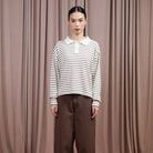 Person wearing a brown and white striped shirt by Hijabchic and brown pants against a beige curtain background