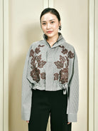 Woman wearing a gray stripe jacket by Studio Tui with floral embroidery against a beige background