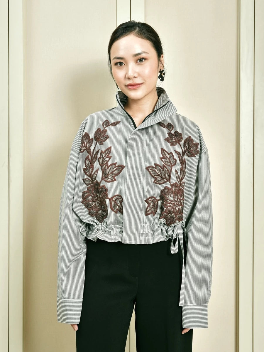 Woman wearing a gray stripe jacket by Studio Tui with floral embroidery against a beige background