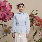 Woman wearing a light blue shirt with floral decorations and 'BWBYAZ' branding.