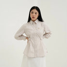 Woman wearing a light-colored blouse by Tunique with a belt against a white background