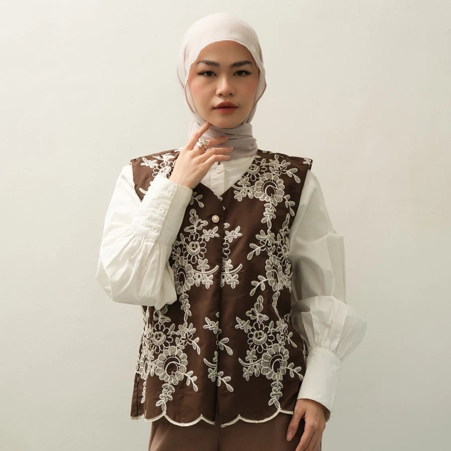 Woman wearing a brown lace vest by Tunique over a white shirt with a plain background