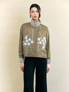 Woman wearing a striped olive-colored shirt by Studio Tui with floral embroidery on a beige background