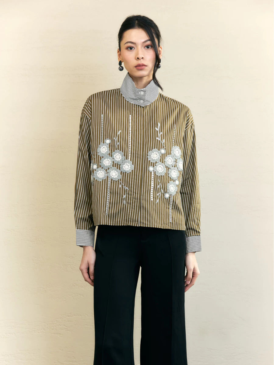 Woman wearing a striped olive-colored shirt by Studio Tui with floral embroidery on a beige background