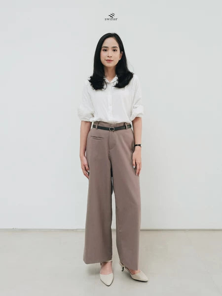 Woman wearing a white blouse and brown pants by Swifter against a white background
