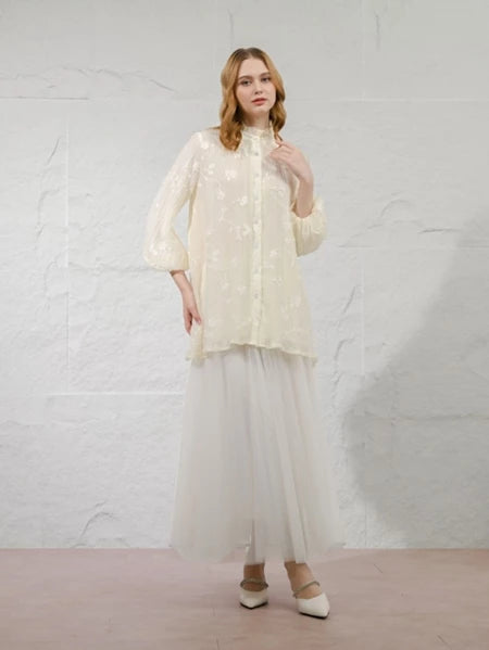 Woman wearing a ivory-colored Della Blouse by Kasa Heritage with a textured top and sheer skirt against a white background
