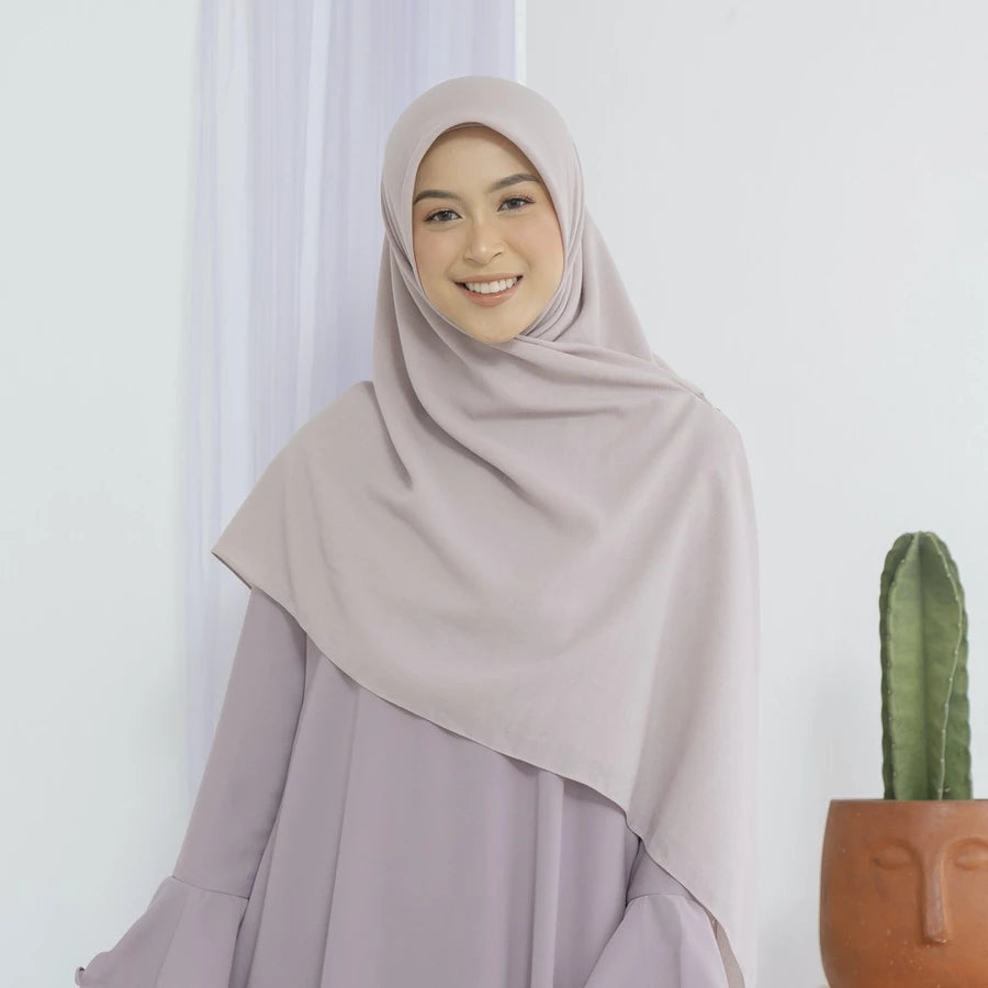 Woman wearing a beige square hijab by Lozy Hijab and dress against a white curtain background