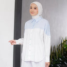 Woman wearing a light blue and white shirt by Casa Elana with a hijab against a gray wall.