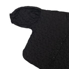 A close-up of a black textured shirt by Yestoday with a crinkled, embossed pattern, featuring a short puff sleeve and a buttoned front, shown on a plain white background.