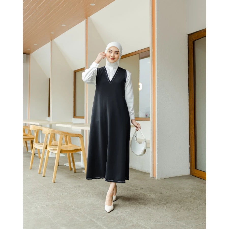 Woman in a black dress by Abame and white hijab standing in a modern interior setting.