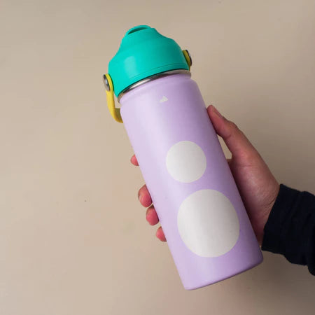 Purple water bottle with white polka dots and a green lid from Muhajir Project held by a hand against a beige background