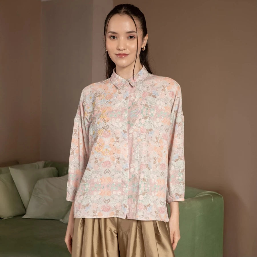Woman wearing a floral blush shirt by Hijabchic standing in a room with a couch.