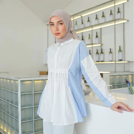 Woman wearing a white and blue striped shirt by Casa Elana with a hijab in an indoor setting.