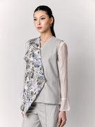 Woman wearing a floral vest by Studio Tui over a light shirt with gray pants on a white background