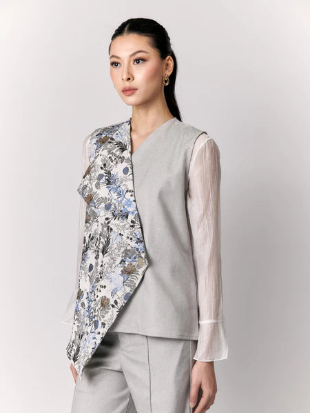 Woman wearing a floral vest by Studio Tui over a light shirt with gray pants on a white background