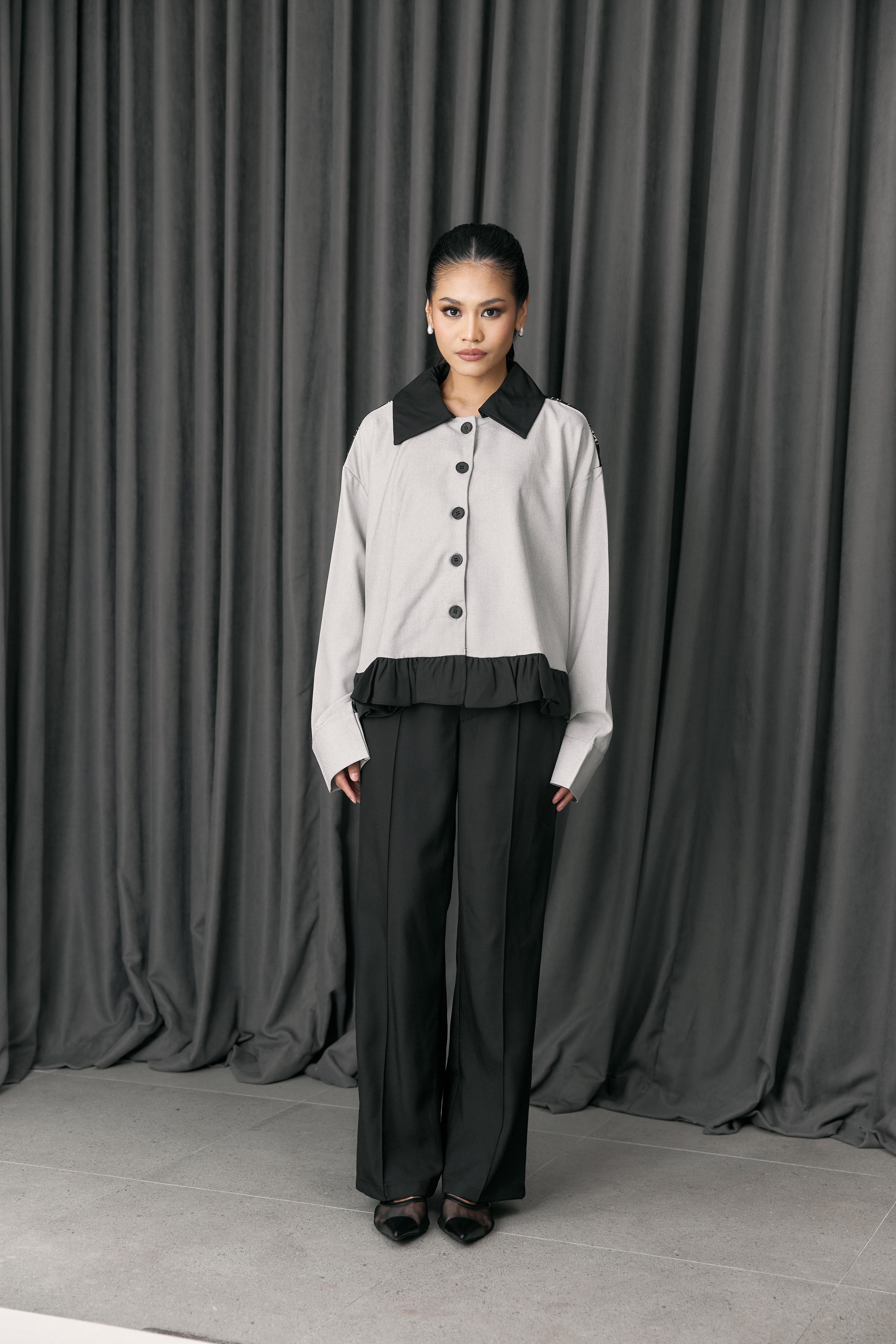 Person wearing a light gray jacket with black accents by Studio Tui and dark pants against a gray curtain background