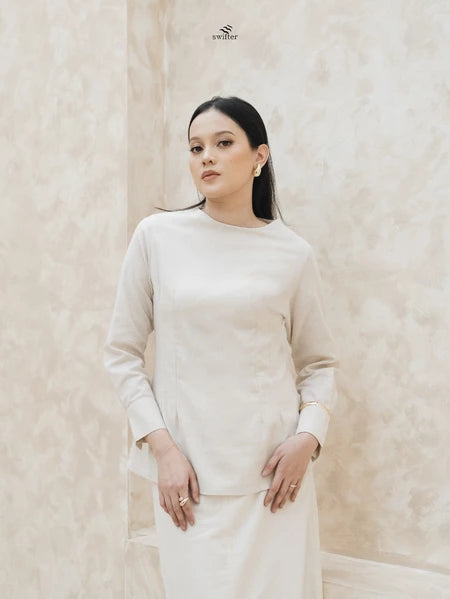 Woman wearing a light brown blouse by Swifter against a beige background