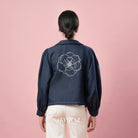 Person wearing a indigo blue jacket by BWBYAZ with a floral design on the back against a pink background