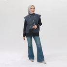 Woman wearing a dark grey vest over a black top and blue jeans on a white background