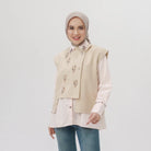 Woman wearing a khaki embroidered vest over a white shirt with a plain background