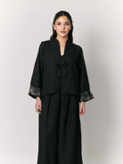 Woman wearing a black outer with floral cuffs by Studio Tui on a white background