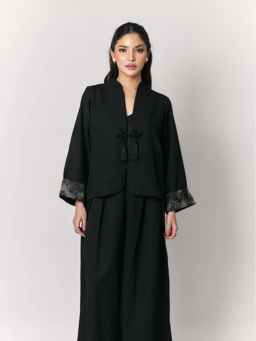 Woman wearing a black outer with floral cuffs by Studio Tui on a white background