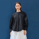 Woman wearing a black patterned puffy shirt against a blue background