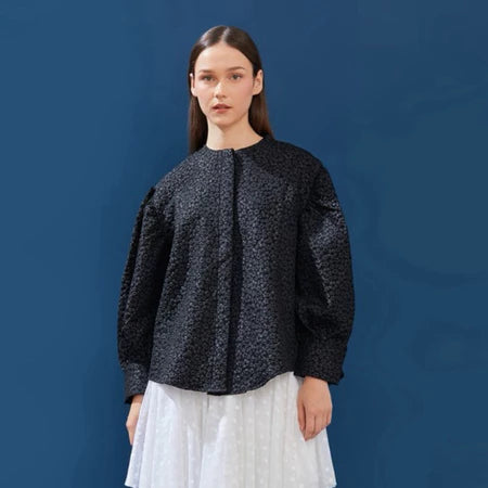 Woman wearing a black patterned puffy shirt against a blue background