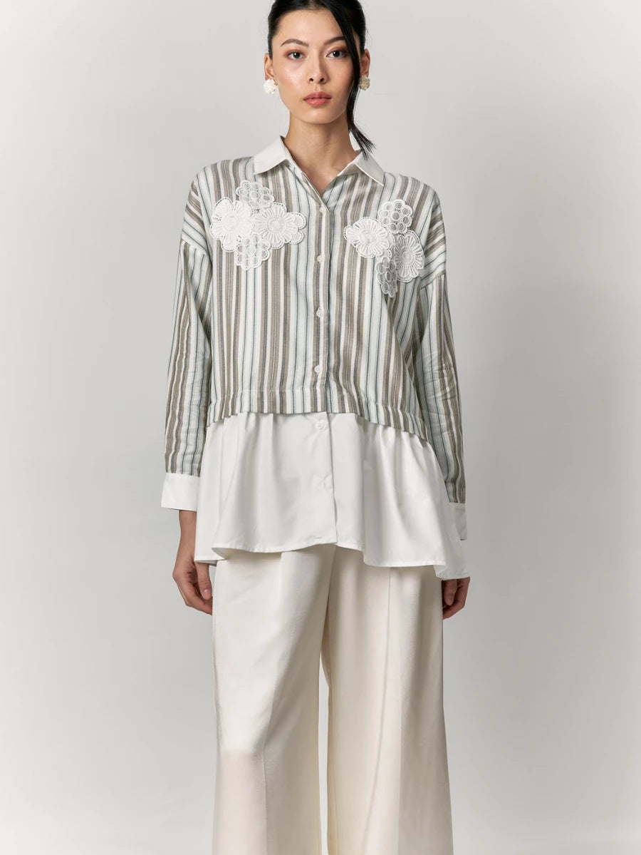Woman wearing a striped shirt by Studio Tui with floral embroidery and white pants on a plain background