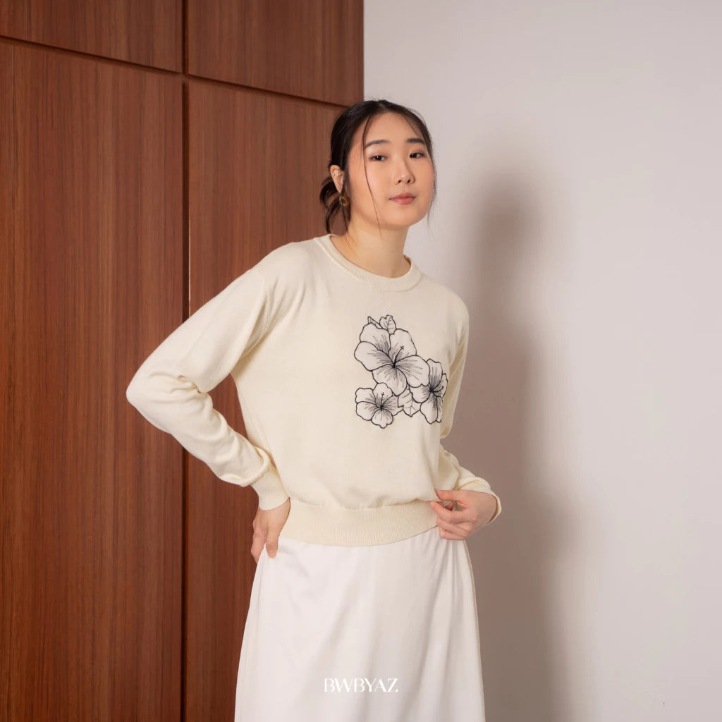 A person wearing a white sweater with a floral embroidery design on the front from BWBYAZ, paired with a white skirt and a white headscarf.