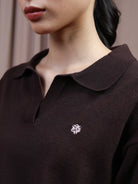 Close-up of a person wearing a dark brown knit polo knit top by Hijabchic with a small white embroidered logo on the chest.