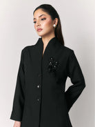 A woman wearing a black blazer by Studio Tui with a stand collar, three front buttons, and a black beaded embellishment on the left chest, photographed against a light gray studio background.