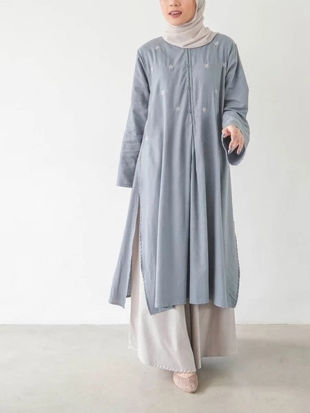 Seorang wanita memakai Fara Tunik, tunik berlengan panjang dengan material soft flanel dan memiliki aksen bunga, berwarna denim.