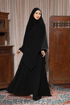 A woman wearing a black abaya set with a headscarf by Lozy Hijab, standing indoors.