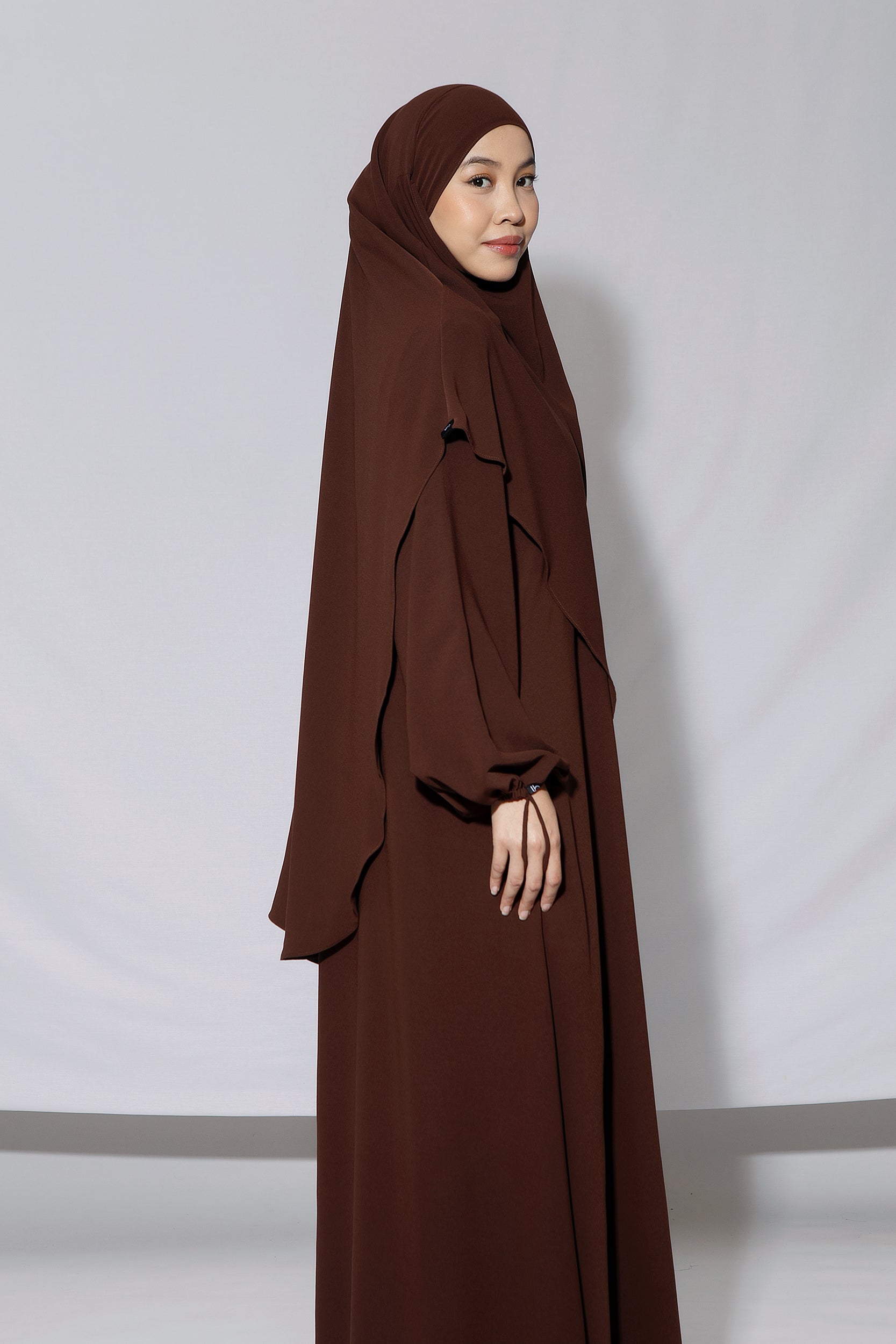 A woman wearing a brown abaya set with a headscarf by Lozy Hijab, standing indoors.