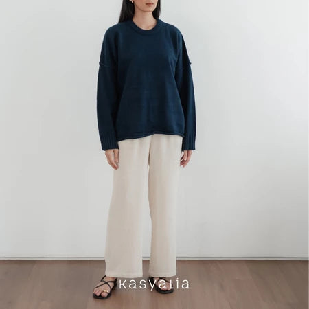 Person wearing a navy oversized sweater and beige pants against a white wall with 'kasyalia' branding.