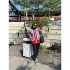 A woman wearing a casual modest shirt by Abame featuring a red base color with gray panels and white ruffle details down the front.