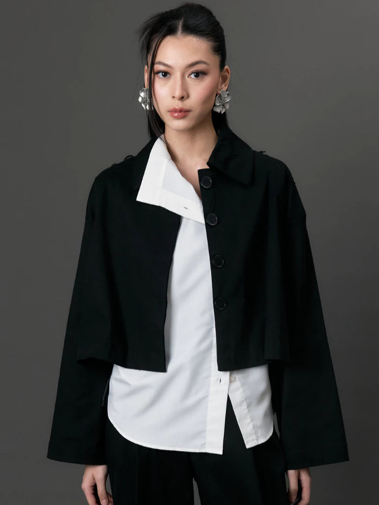 Woman wearing a black coat by Studio Tui over a white shirt on a gray background
