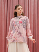Woman wearing a floral pink blouse by Kasa Heritage against a pink curtain background