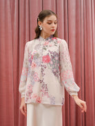 Woman wearing a floral beige blouse by Kasa Heritage against a pink curtain background