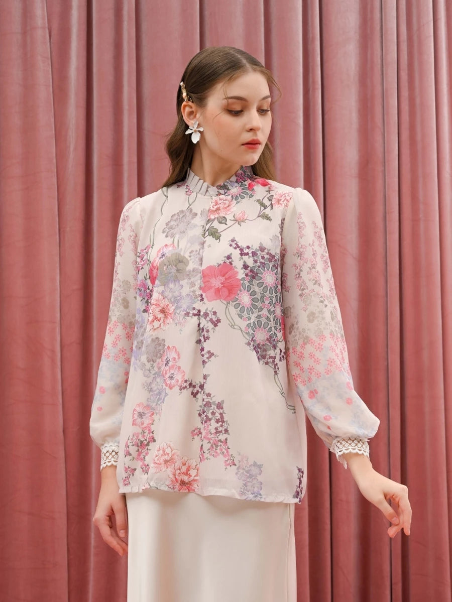 Woman wearing a floral beige blouse by Kasa Heritage against a pink curtain background