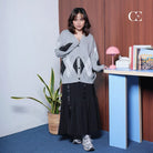 A person standing in a room wearing a grey fir cardigan by Casa Elana over a black top, paired with a long black skirt and white sneakers.
