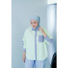 Woman wearing a light green shirt with striped sleeves and a matching hijab against a white background