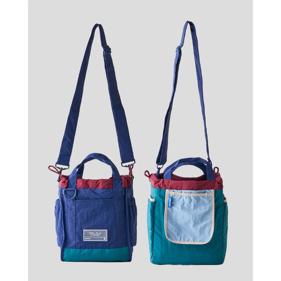 Women’s reversible tote bag by Muhajir Project featuring two looks in one design. One side comes in navy blue with teal accents and a clean front pocket, while the other side shows a teal body with a contrasting light blue pocket. Designed with adjustable shoulder straps, top handles, and side drawstring details for a practical and versatile everyday bag.